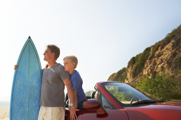 Vater und Sohn mit Surfbrett am Auto gegen den Himmel - CAVF13973