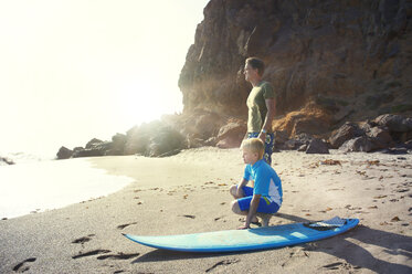 Vater und Sohn mit Surfbrett am Meeresufer am Strand an der Klippe - CAVF13975