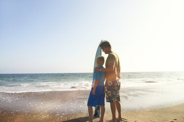 Vater und Sohn mit Surfbrett am Meer am Strand gegen klaren Himmel - CAVF13976