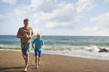 Vater und Sohn laufen am Strand an einem sonnigen Tag - CAVF13980