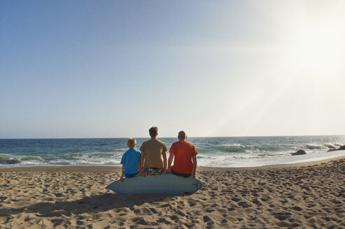 Rückansicht einer Familie, die auf einem Surfbrett am Strand sitzt, gegen einen klaren Himmel an einem sonnigen Tag - CAVF13983