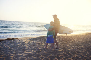 Älterer Mann hält Surfbrett und steht mit Enkel am Strand - CAVF13989