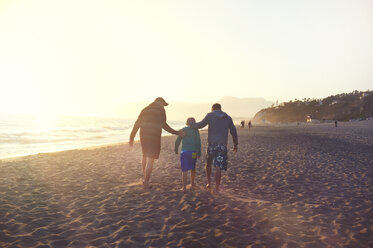 Rear view of family walking at beach against clear sky during sunset - CAVF13991