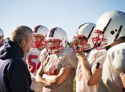 Trainer im Gespräch mit American-Football-Spielern an einem sonnigen Tag, lizenzfreies Stockfoto