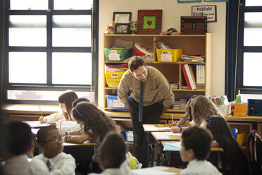 Lehrer schaut zu den Kindern, die an den Tischen im Klassenzimmer sitzen - CAVF14016