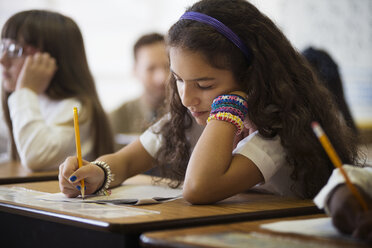 Schülerin beim Schreiben eines Tests, während sie am Schreibtisch im Klassenzimmer sitzt - CAVF14018