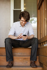 Glücklicher Mann telefoniert auf einer Treppe sitzend - CAVF14031