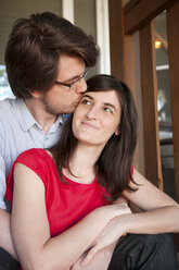 Man kissing girlfriend while sitting by railing - CAVF14033