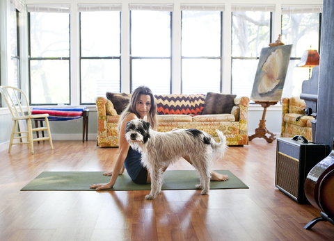 Porträt einer Frau, die mit ihrem Hund zu Hause auf einer Trainingsmatte sitzt, lizenzfreies Stockfoto