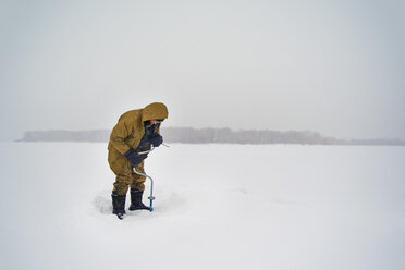 Älterer Mann bohrt in gefrorenem See vor klarem Himmel - CAVF14044