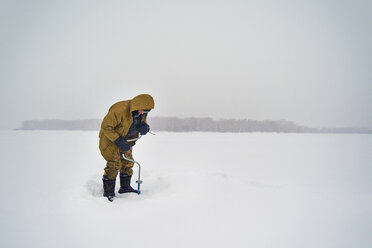 Senior man drilling in frozen lake against clear sky - CAVF14044