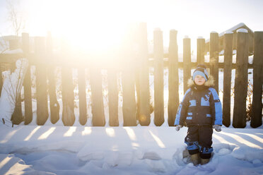 Porträt eines Jungen, der an einem sonnigen Tag auf einem schneebedeckten Feld vor einem Zaun steht - CAVF14067