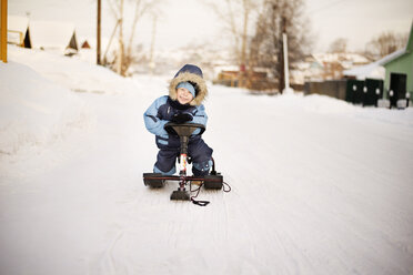 Porträt eines glücklichen Jungen, der im Winter auf einem Schlitten sitzt - CAVF14071