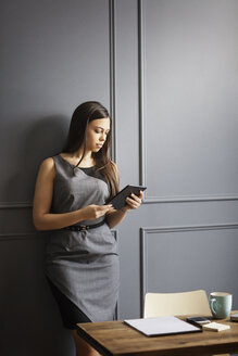 Geschäftsfrau, die einen Tablet-Computer benutzt und sich im Büro an die Wand lehnt - CAVF14078