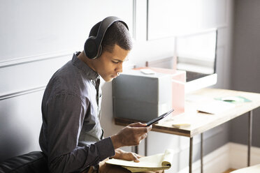 Seitenansicht eines Geschäftsmannes, der Musik hört, während er einen Tablet-Computer im Büro benutzt - CAVF14083