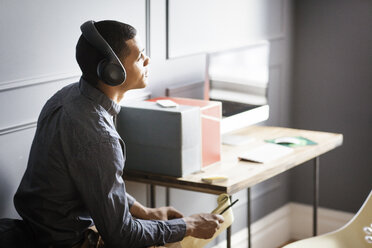 Businessman looking away while listening music in office - CAVF14084