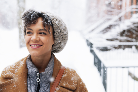 Lächelnde Frau, die wegschaut, während sie auf einem schneebedeckten Feld geht, lizenzfreies Stockfoto