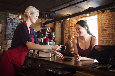 Seitenansicht einer Frau, die einem Kunden in einem Cafe Kaffee serviert - CAVF14099