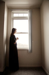 Side view of woman looking away while standing by window at home - CAVF14117