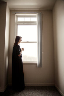 Seitenansicht einer Frau, die wegschaut, während sie zu Hause am Fenster steht - CAVF14117