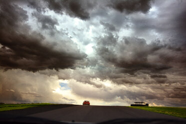 Bewölkter Himmel über einer Straße inmitten eines grasbewachsenen Feldes, gesehen durch die Windschutzscheibe eines Autos - CAVF14123