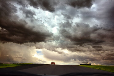 Cloudy sky over street amidst grassy field seen through car windshield - CAVF14123