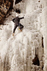 Mann klettert an gefrorenem Wasserfall gegen Felsformation - CAVF14138