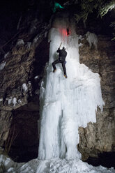 Niedriger Blickwinkel eines Eiskletterers, der auf einen gefrorenen Wasserfall klettert - CAVF14145