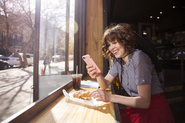 Glückliche Frau schaut in einem Café auf ihr Telefon - CAVF14174