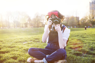 Frau mit gekreuzten Beinen fotografiert durch die Kamera, während sie im Park sitzt - CAVF14189