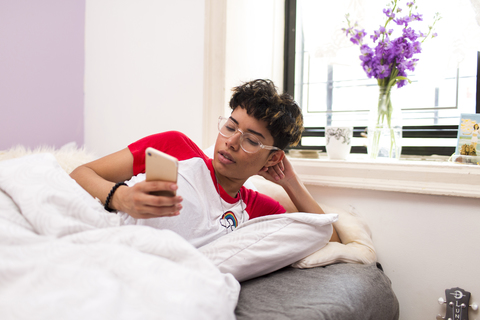 Junge Frau, die im Bett liegend ein Mobiltelefon benutzt, lizenzfreies Stockfoto