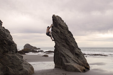 Seitenansicht eines Mannes, der eine Felsformation gegen einen bewölkten Himmel erklimmt - CAVF14216