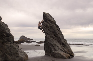 Side view of man climbing rock formation against cloudy sky - CAVF14216