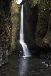 Rückansicht eines Mannes ohne Hemd, der vor einem Wasserfall steht - CAVF14218