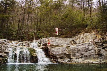 Männliche Freunde springen in den See gegen eine Felsklippe am Waldrand - CAVF14233