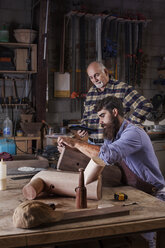 Älterer Mann betrachtet einen Arbeiter, der in einer Werkstatt Holz schnitzt - CAVF14380
