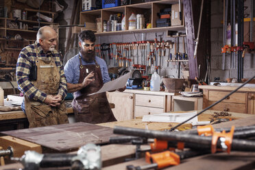 Craftsmen discussing work with senior man while standing at workshop - CAVF14391