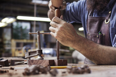 Ausgeschnittenes Bild eines Arbeiters, der in einer Holzwerkstatt Werkzeuge in Bretter hämmert - CAVF14398