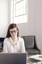 Confident businesswoman using laptop while sitting in office - CAVF14409