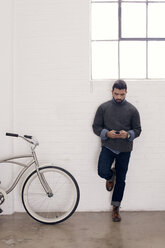 Businessman using phone while leaning against wall at creative office - CAVF14410