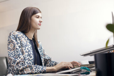 Serious businesswoman typing on computer keyboard by wall at office - CAVF14413