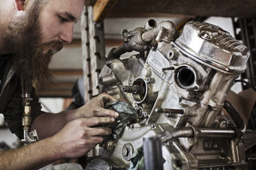 Ausgeschnittenes Bild eines Mechanikers, der in einer Werkstatt an einem Motorradmotor arbeitet - CAVF14421