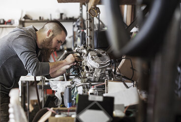 Seriöser Mechaniker arbeitet an einem Motorradmotor in einer Autowerkstatt - CAVF14422