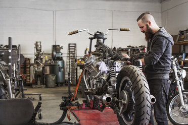 Seriöser Mechaniker bei der Arbeit an einem Motorrad in einer Reparaturwerkstatt - CAVF14423