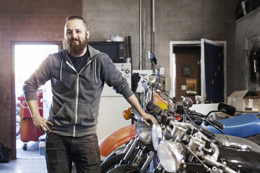 Portrait of confident mechanic standing by motorcycles at shop - CAVF14425