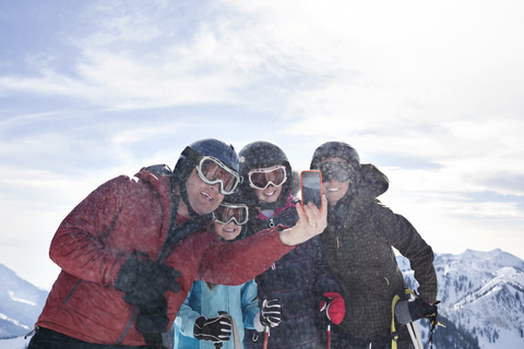 Familie, die ein Selfie mit ihrem Smartphone macht, während sie am Skiberg steht, lizenzfreies Stockfoto