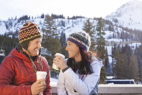 Happy couple having coffee while standing against snowcapped mountains - CAVF14468