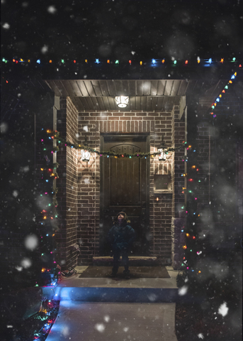 Junge in warmer Kleidung steht nachts am Eingang, lizenzfreies Stockfoto