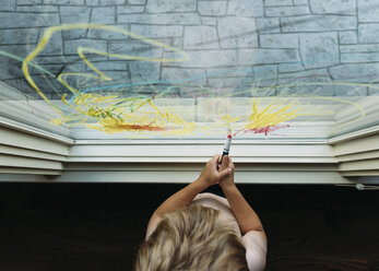 Junge malt mit Buntstift am Fenster zu Hause - CAVF14502