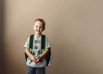 Porträt eines glücklichen Jungen mit Rucksack, der zu Hause an der Wand steht - CAVF14505